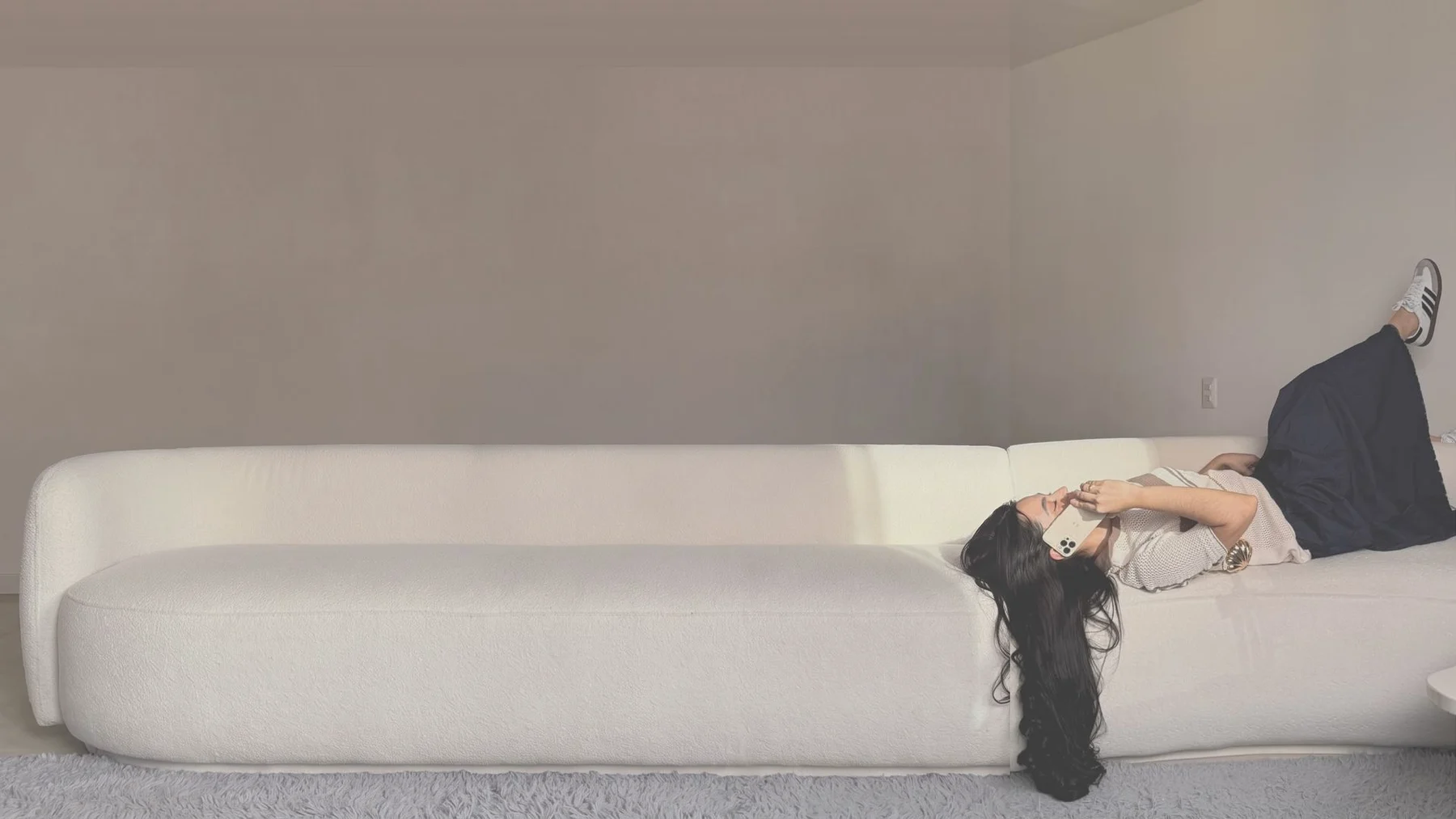 Modelo recostada en un sofá blanco de una sala, con top tejido color crema y pantalón ancho azul oscuro
